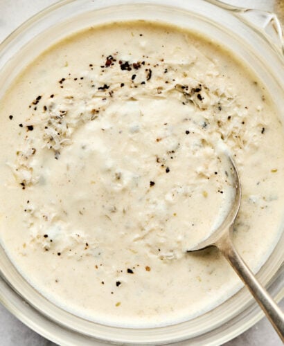 A close-up overhead shot of mixed Greek yogurt caesar dressing in a glass bowl atop a white marbled surface.