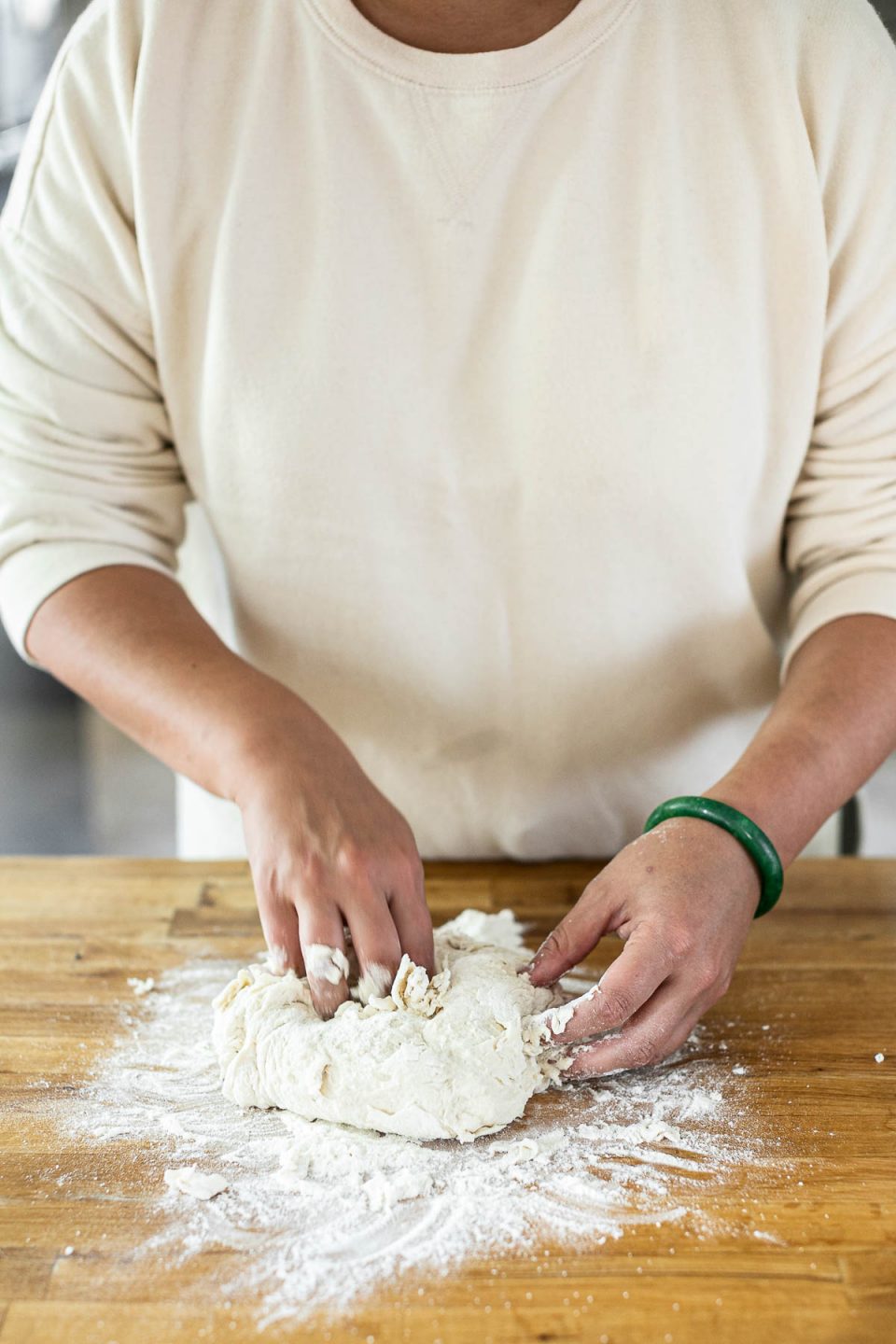 Mixing DeLallo Pizza Dough Kit: Jess, shown in a white sweatshirt, stands behind a butcher block counter, kneading the pizza dough with her hands.