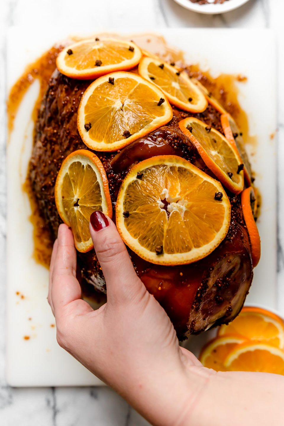 Woman's hands shown studding thinly sliced oranges on ham with whole cloves.