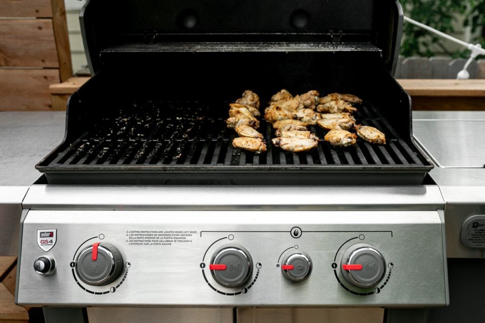 Grilled Lemony Greek Chicken Wings sit on top of Weber Grill grates over direct heat. The grill burners are set to high heat to help the wings develop crispy char marks & flavor.