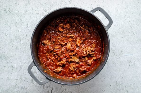 Braised lamb ragu in a large Dutch oven atop a light blue surface.