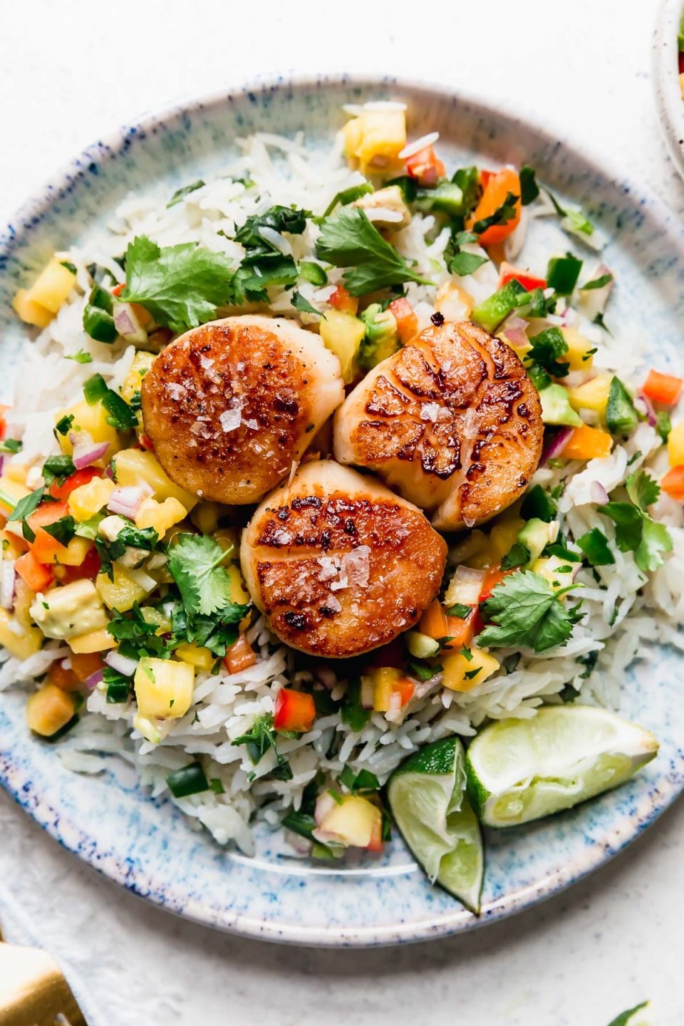 3 seared scallops served on a blue plate with coconut rice & mango salsa. The easiest healthy seared scallops recipe!