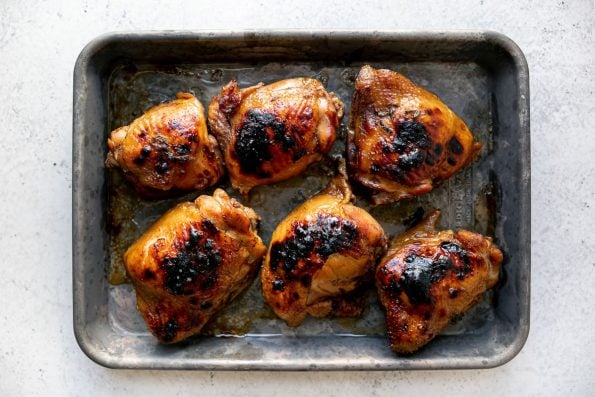 Broiled shoyu chicken thighs on a small Nordicware baking sheet, atop a white surface.