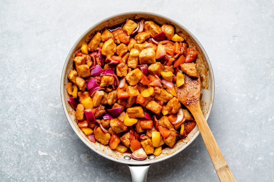 Stir fried pork & veggies in sweet & sour sauce in a large skillet with a wooden spoon.